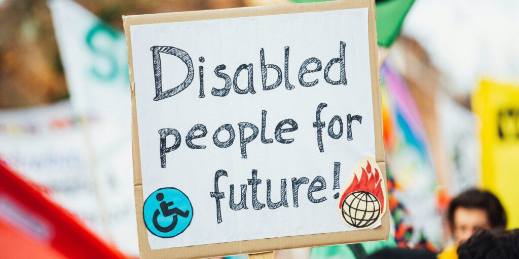 A close up of a poster at a protest that says disabled people for the future and includes an icon of the earth on fire