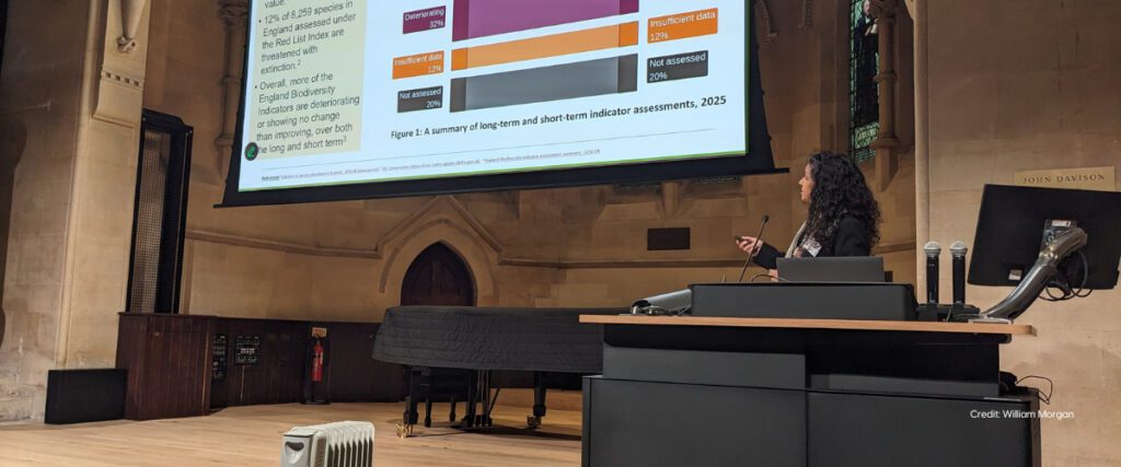 A close up of a woman presenter who is talking to a large slide
