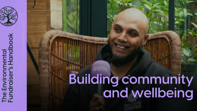 A bald, brown man with a black beard and a black hoodie, is speaking into a purple microphone with the EFN logo on whilst sitting in a wicker chair in a greenhouse. Purple writing over the top says Building community and wellbeing and The Environmental Fundraiser's Handbook.