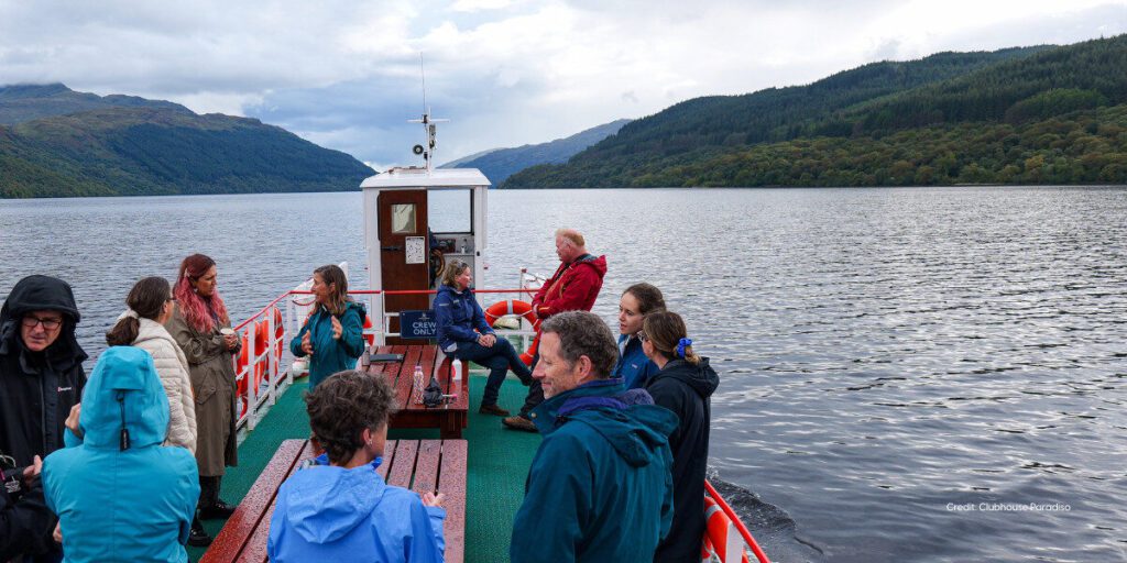 A group of funders are chatting on a small boat on Loch Lomond on bright day