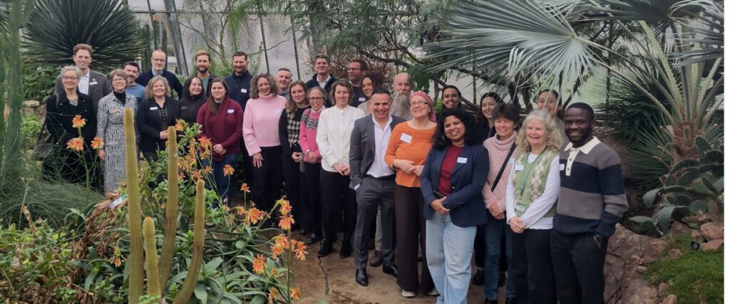 A mixed group of about 30 men and women are smiling to the camera in a bright and vibrant botanical garden.