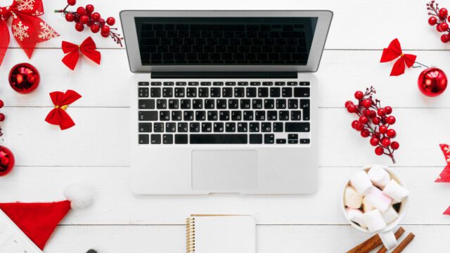 A laptop is on a white desk with lots of red christmas decorations surrounding it.