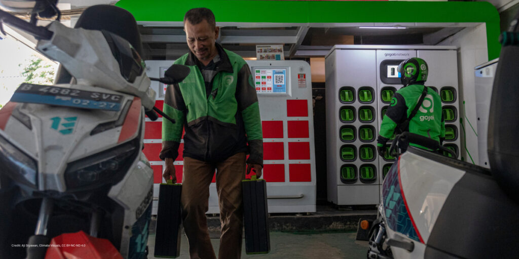 A male driver with brown skin and brown short hair carries a lithium-ion battery at the swapping station to his motorbike.
