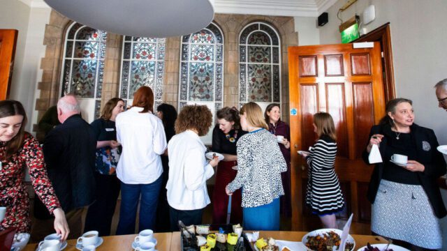 A group of fundraisers are mingling around drinking coffee and chatting in small groups