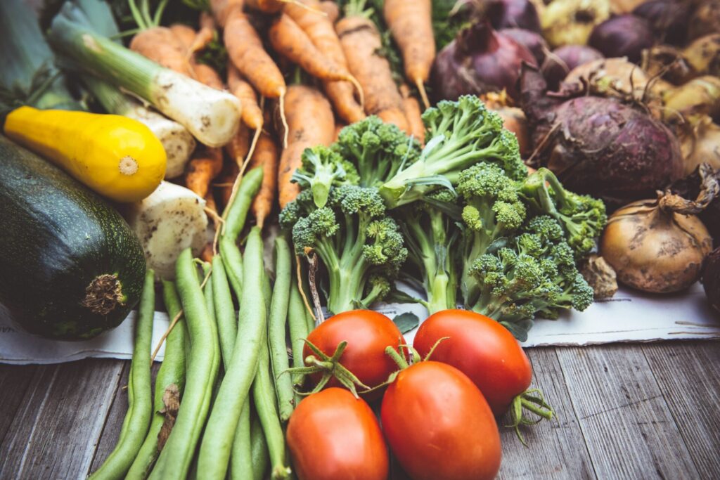 A selection of fresh vegetables are sitting on a grey kitchen table, including green beans, tomatoes, carrots, onions and more
